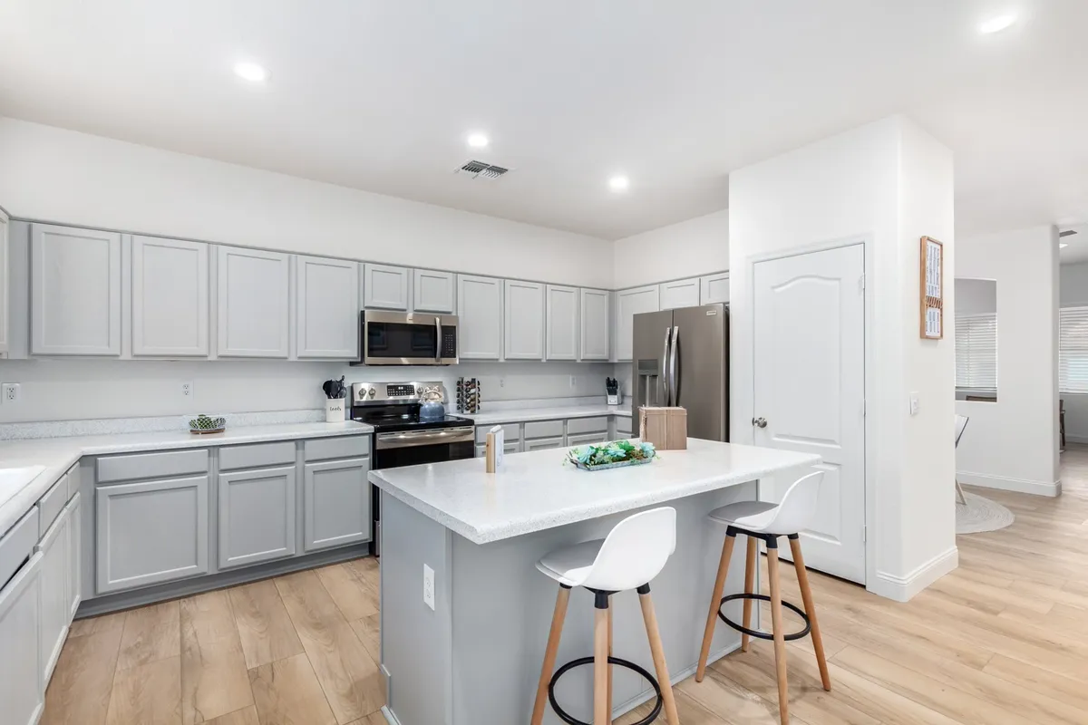 A bright and welcoming kitchen scene with a prominent island, modern stainless steel appliances, bar stools for casual seating, and plenty of counter space. The arrangement encourages family interaction and socializing while cooking or enjoying snacks together.