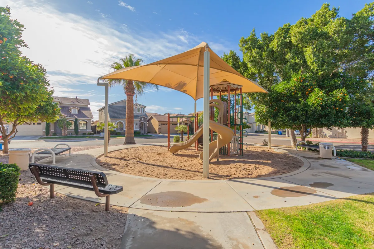 A well-equipped community playground with modern play structures, a shade canopy, a sandy play area, and benches for families to sit and watch children play. The environment feels safe and welcoming, perfect for neighborhood gatherings.
