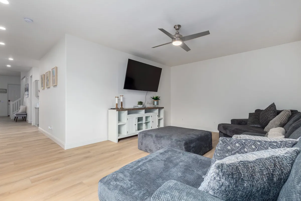 A contemporary living space with a large sectional sofa, flat-screen TV, coffee table, and decorative plant. The room exudes comfort and style, ideal for unwinding or catching up on work with fast WiFi after a busy day.