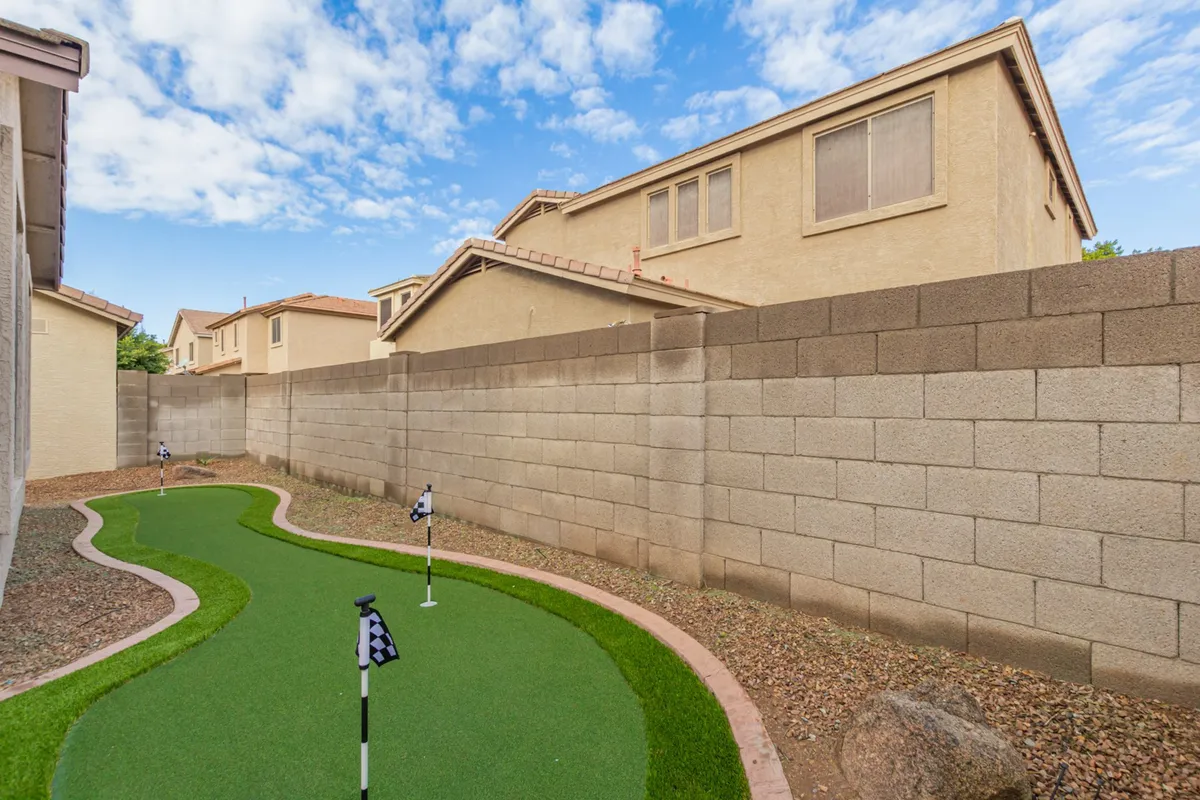 This image showcases a well-maintained backyard putting green bordered by attractive landscaping and an open sky above. The putting green is the focal point, inviting both golf practice and leisurely outdoor relaxation.