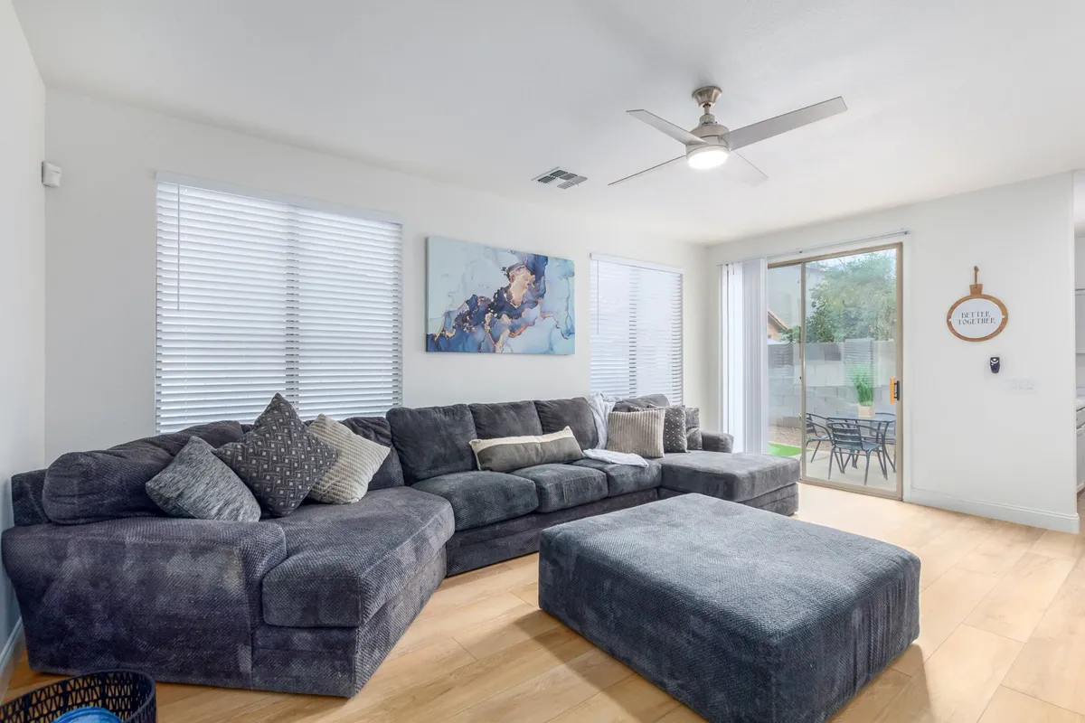 A comfortable interior scene with a large sectional sofa, artwork on the wall, and a sliding glass door leading directly to the outdoor space. The room is bright and inviting, suggesting a seamless indoor-outdoor lifestyle.